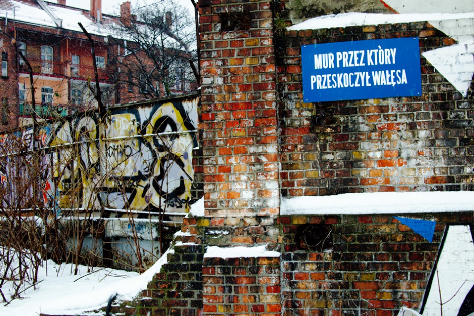 Mur Stoczni Gdańskiej z tablicą upamiętniającą historyczny skok Lecha Wałęsy, którym lider Solidarności dostał się na teren strajkującego zakładu, źródło: wikipedia.org/CC BY 2.0.